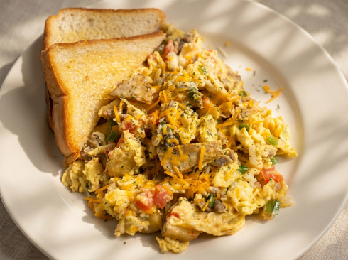 A plate of scrambled eggs with melted cheese, diced vegetables, and pieces of meat, served with two slices of toast.