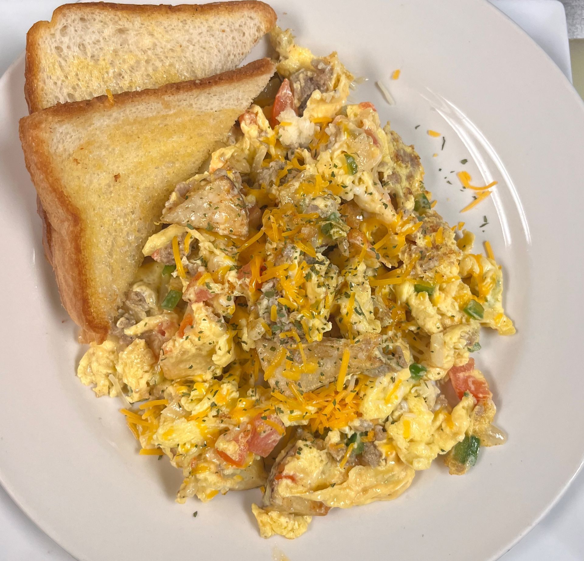 Scrambled eggs with diced sausage, peppers, and melted cheese, served with two slices of toasted bread on a white plate.