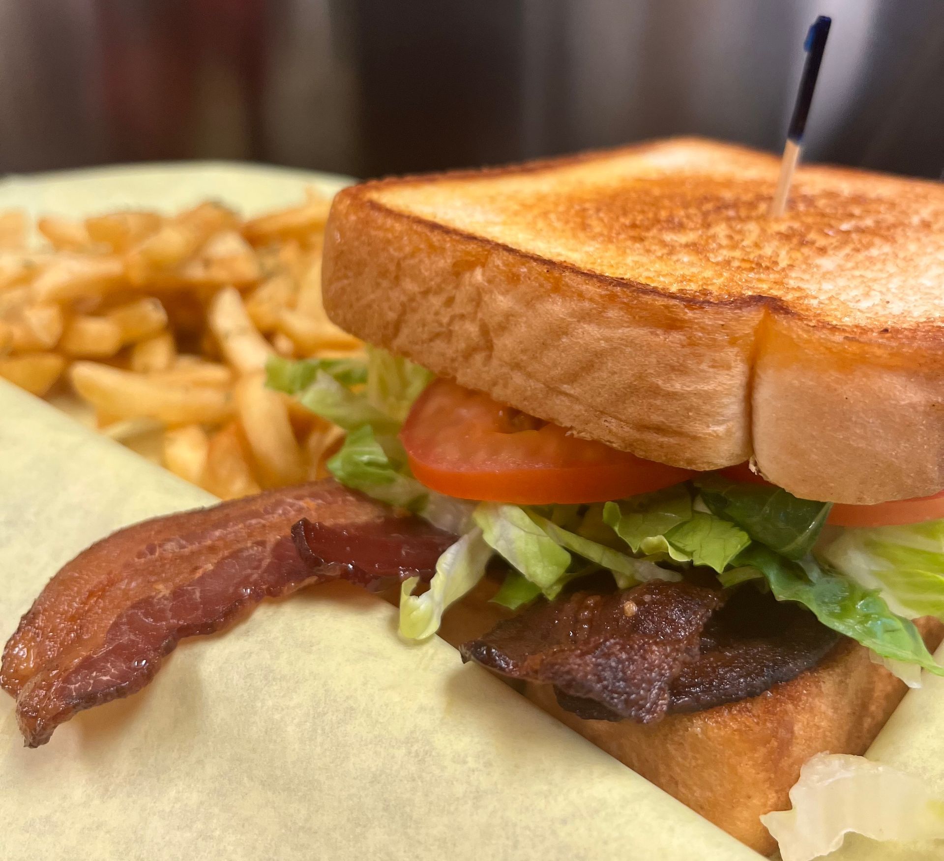 A BLT sandwich with toasted bread and crispy bacon, served with a side of french fries on a parchment-lined plate.