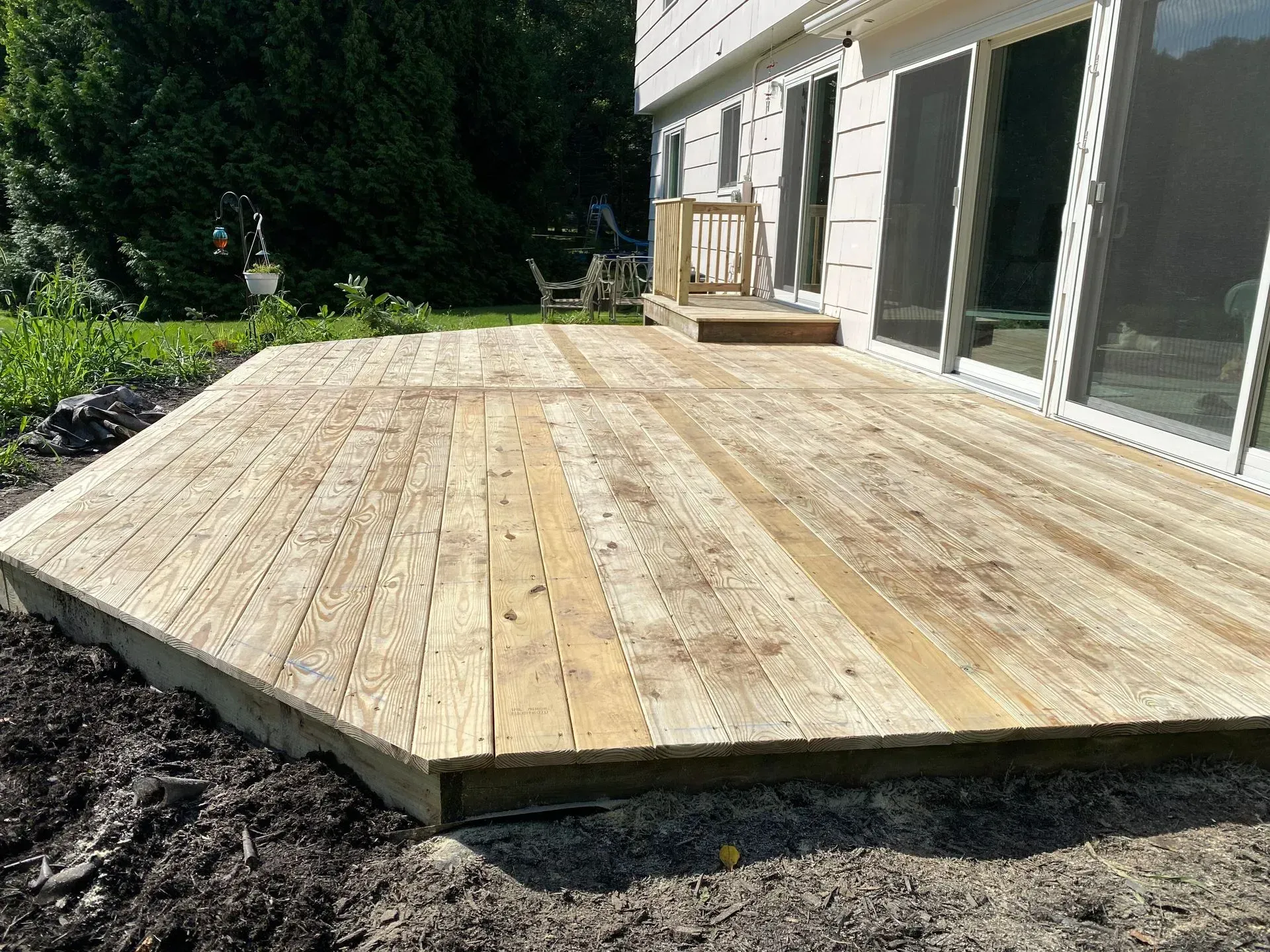 A wooden deck is sitting in the dirt in front of a house.