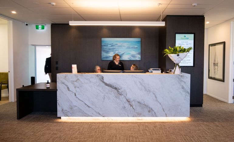 Modern hotel reception desk with marble front, two staff behind it, and a framed seascape on the wall