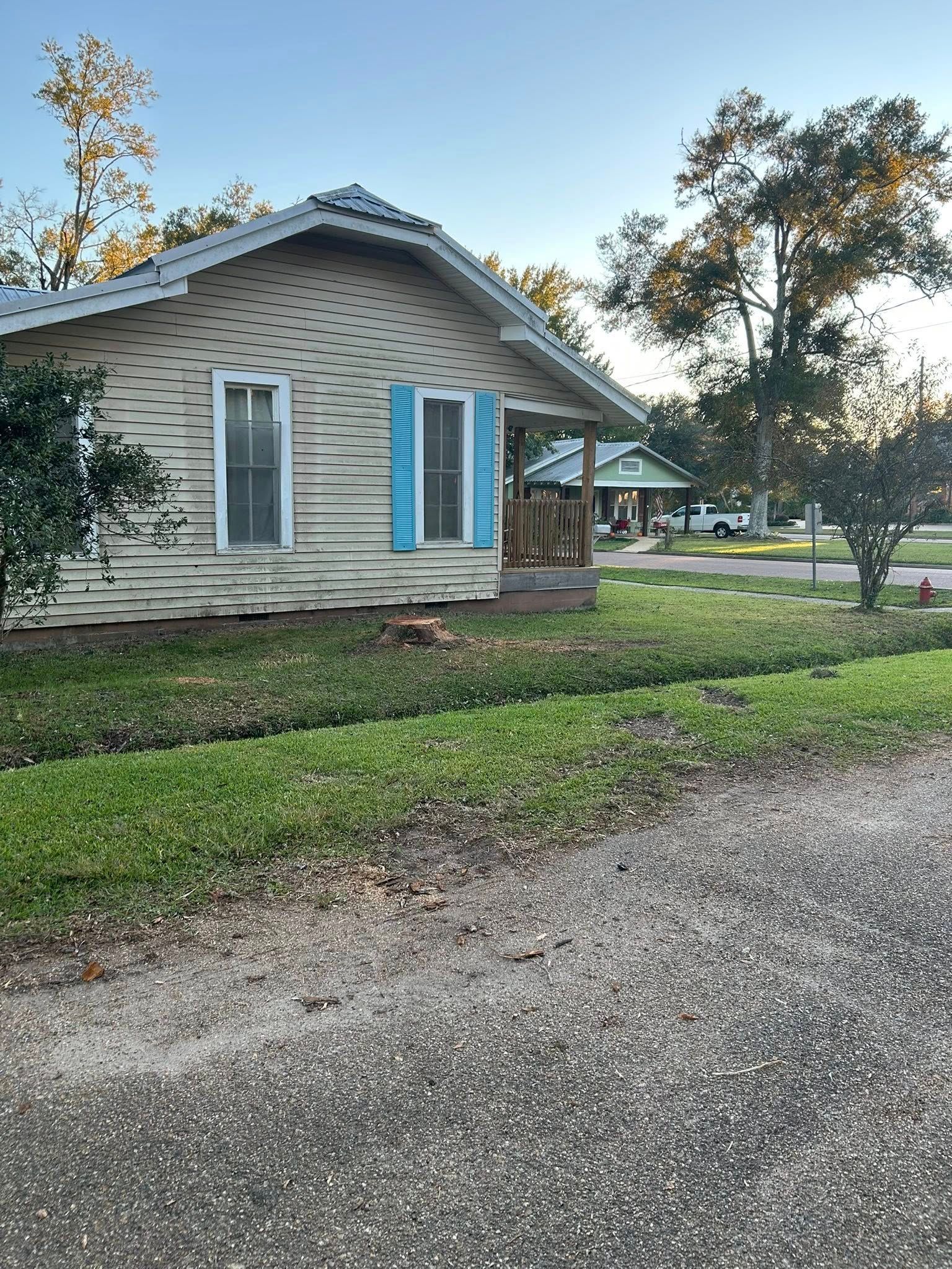 Small beige house with blue shutters beside a gravel driveway and green lawn at dusk