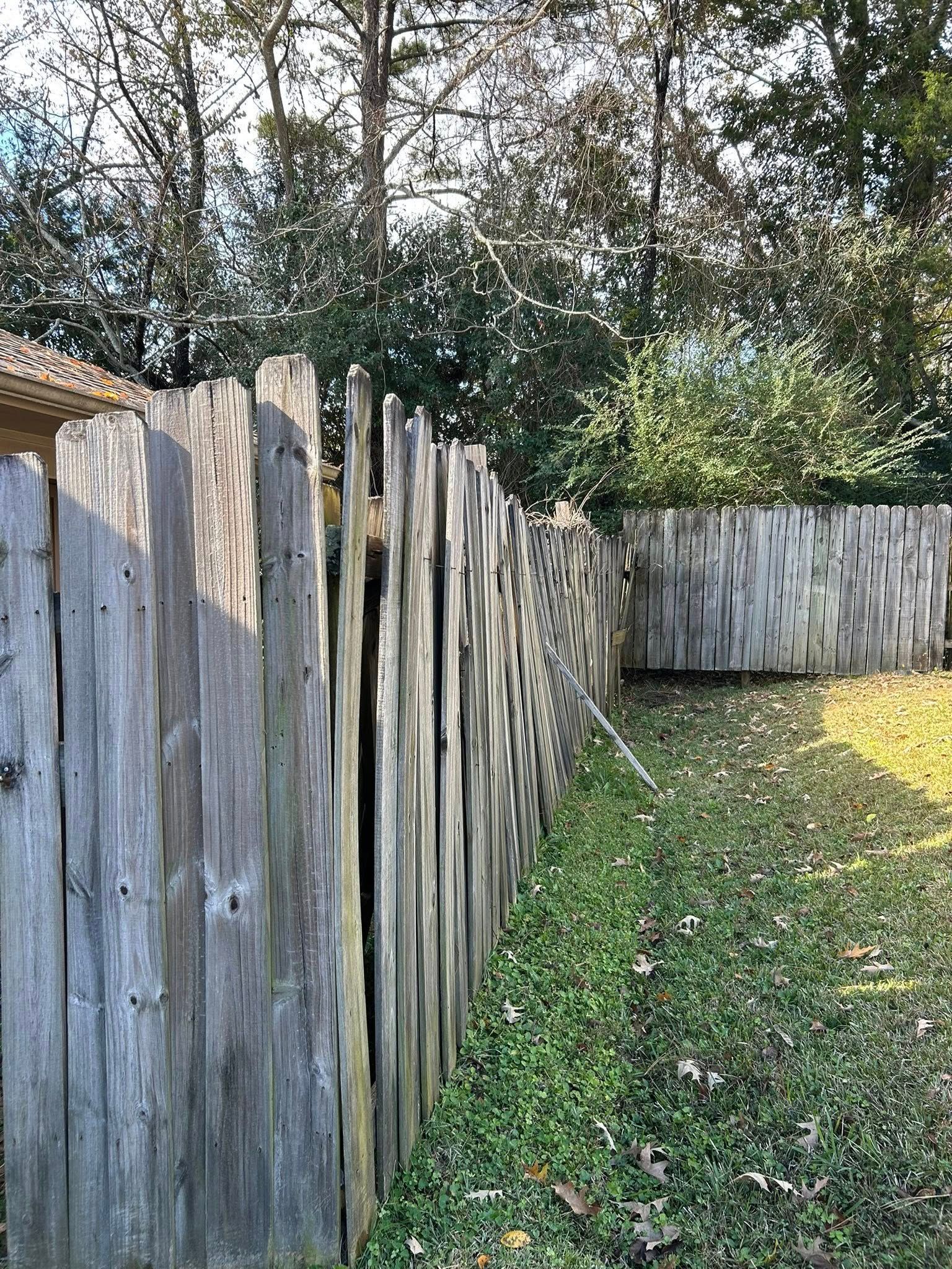 Weathered wooden fence bordering a grassy yard with trees in the background