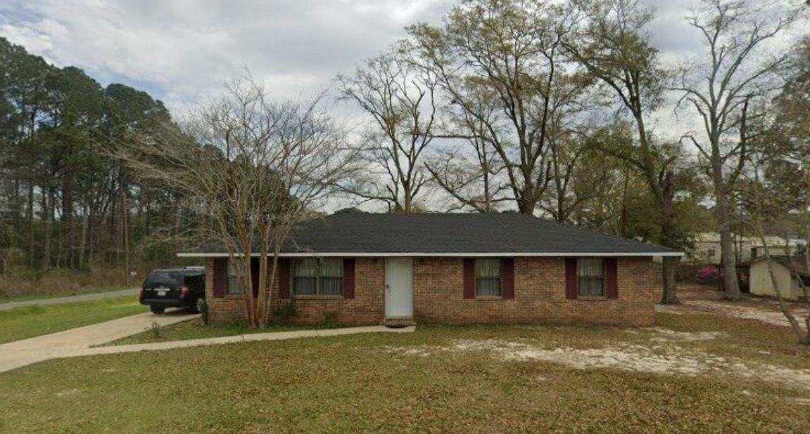 Red brick house with black roof, green lawn, and bare trees under a cloudy sky.