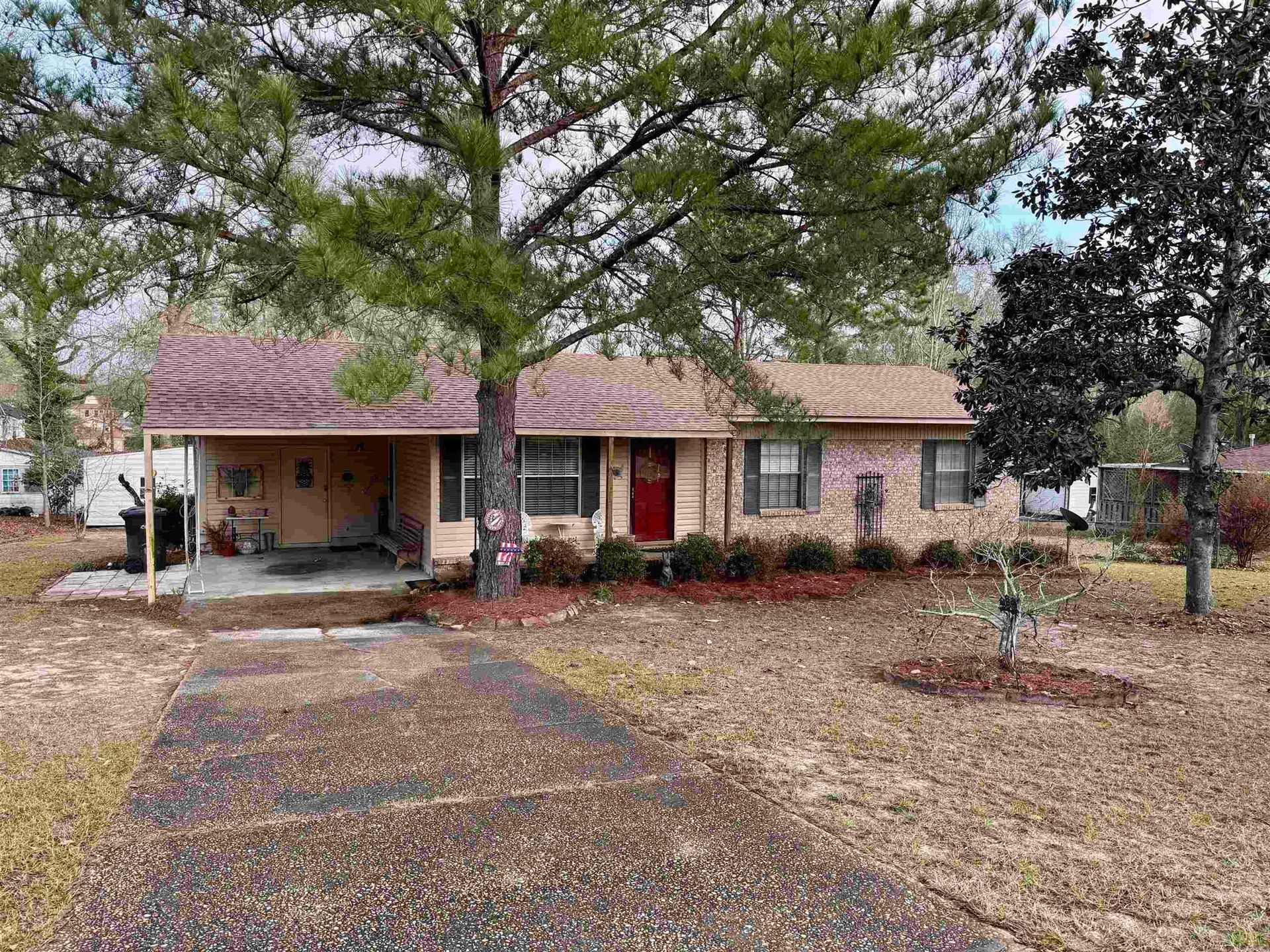 Ranch-style house with red door, brick facade, covered porch, and driveway. Trees and landscaping in front.