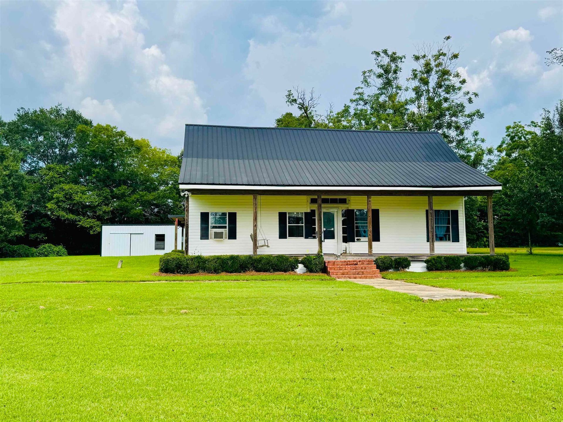 White house with black shutters and a metal roof on a green lawn.