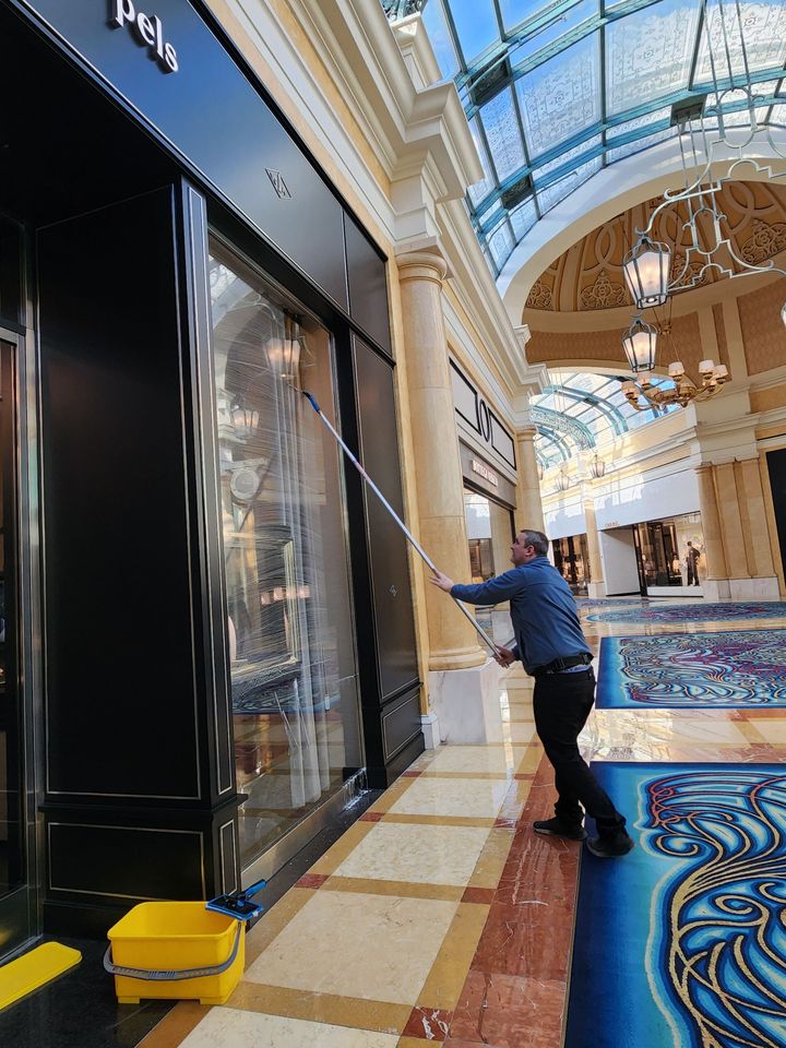 Worker cleaning a black storefront under an ornate arched ceiling in a luxury mall