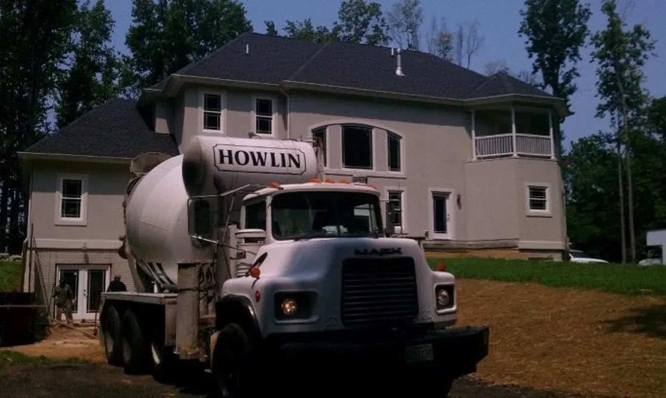 A howlin cement truck is parked in front of a large house