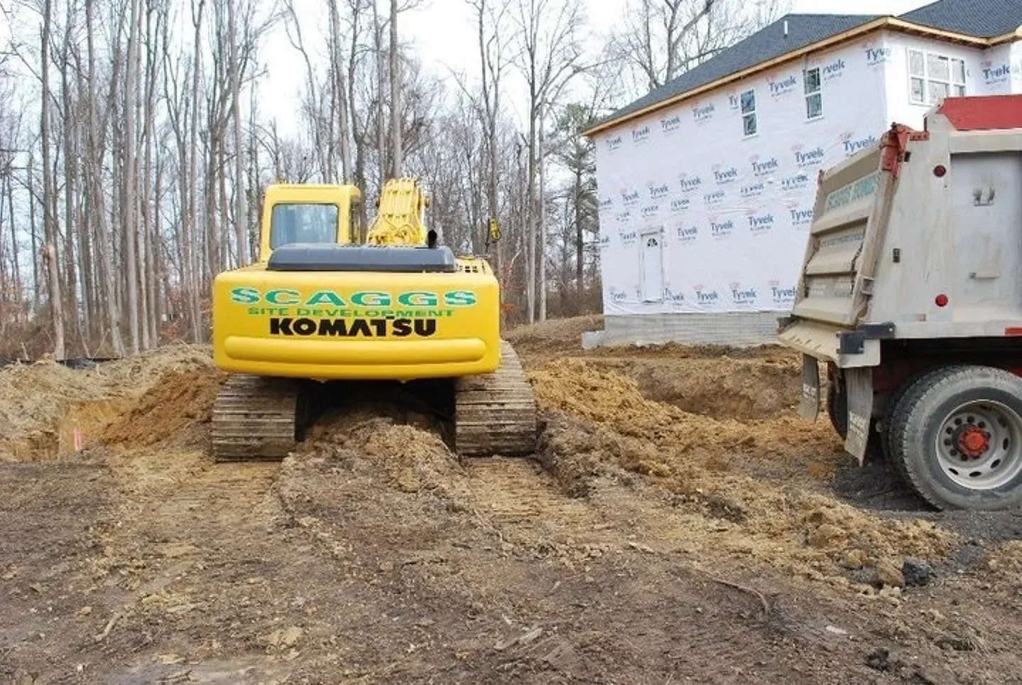 A yellow komatsu excavator is parked next to a dump truck