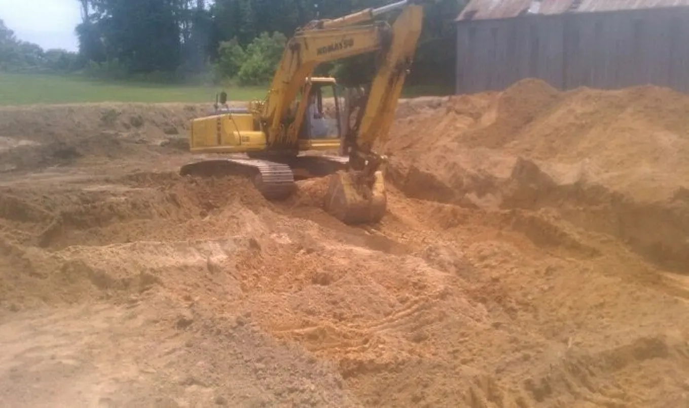 A yellow excavator is digging a hole in a pile of dirt.