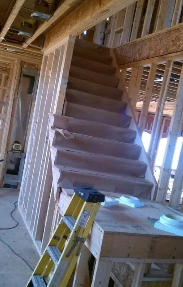 A yellow ladder is sitting next to a wooden staircase in a house under construction.