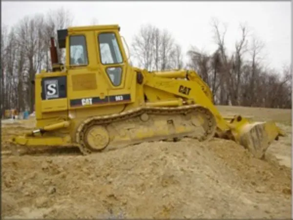 A yellow Caterpillar tracked loader sits on a dirt mound in an outdoor, overcast setting.