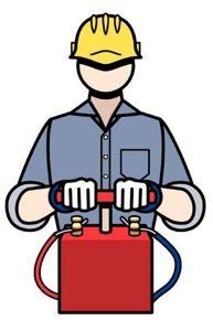 A worker wearing a yellow hard hat presses down on the handle of a red, box-shaped blasting machine.