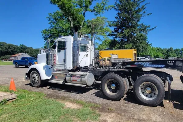A white semi truck with a trailer attached to it is parked in a parking lot.