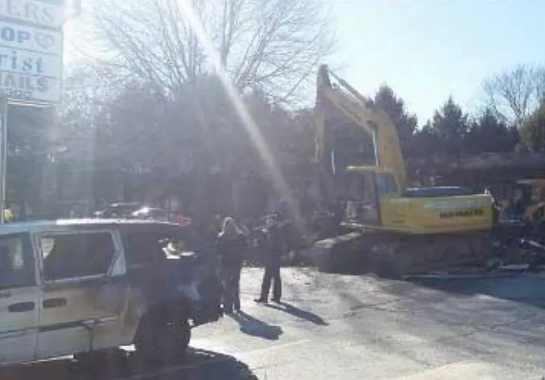 A group of people are standing in front of a large yellow excavator.