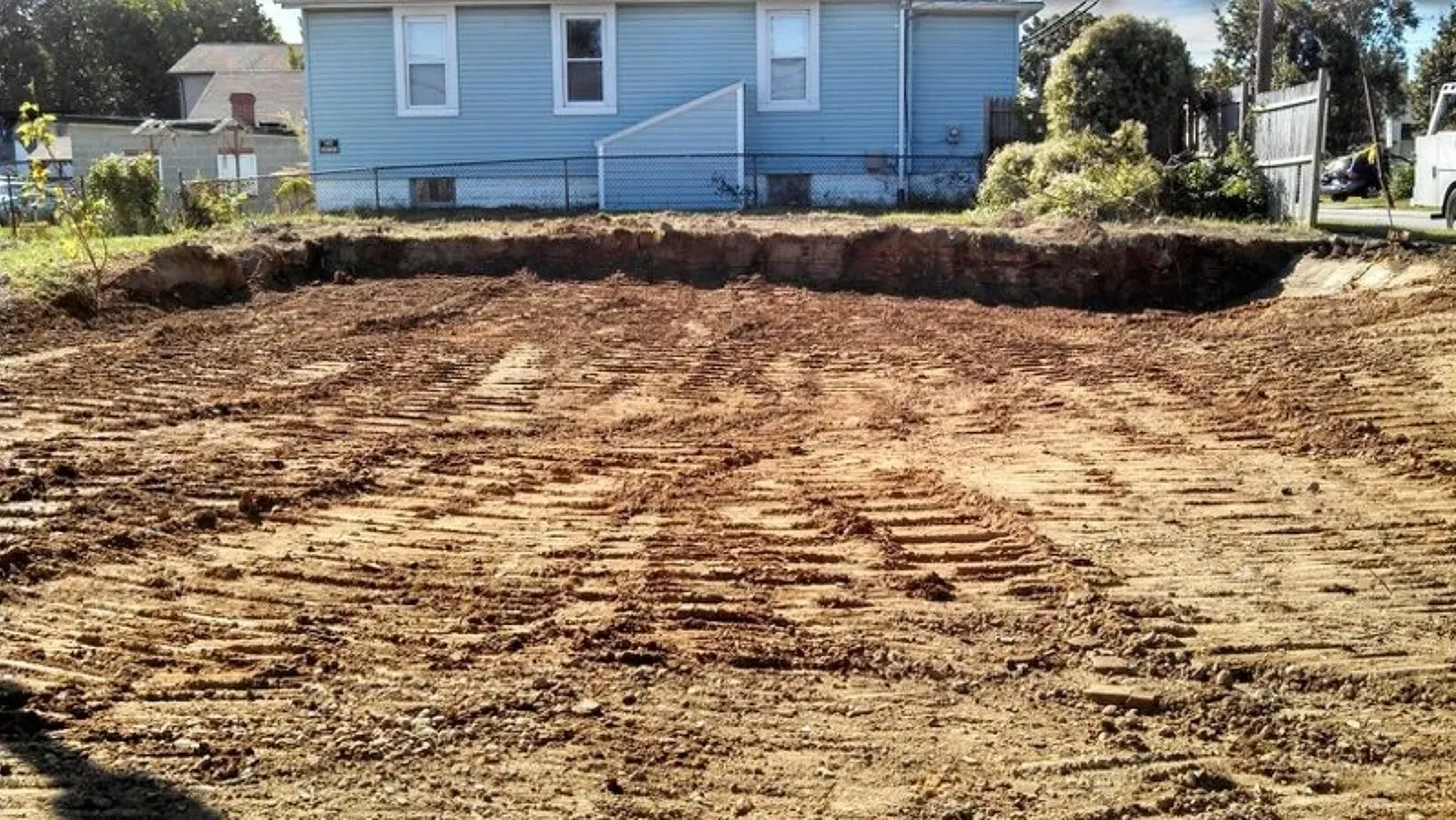 A large pile of dirt in front of a blue house after a lot clearing.