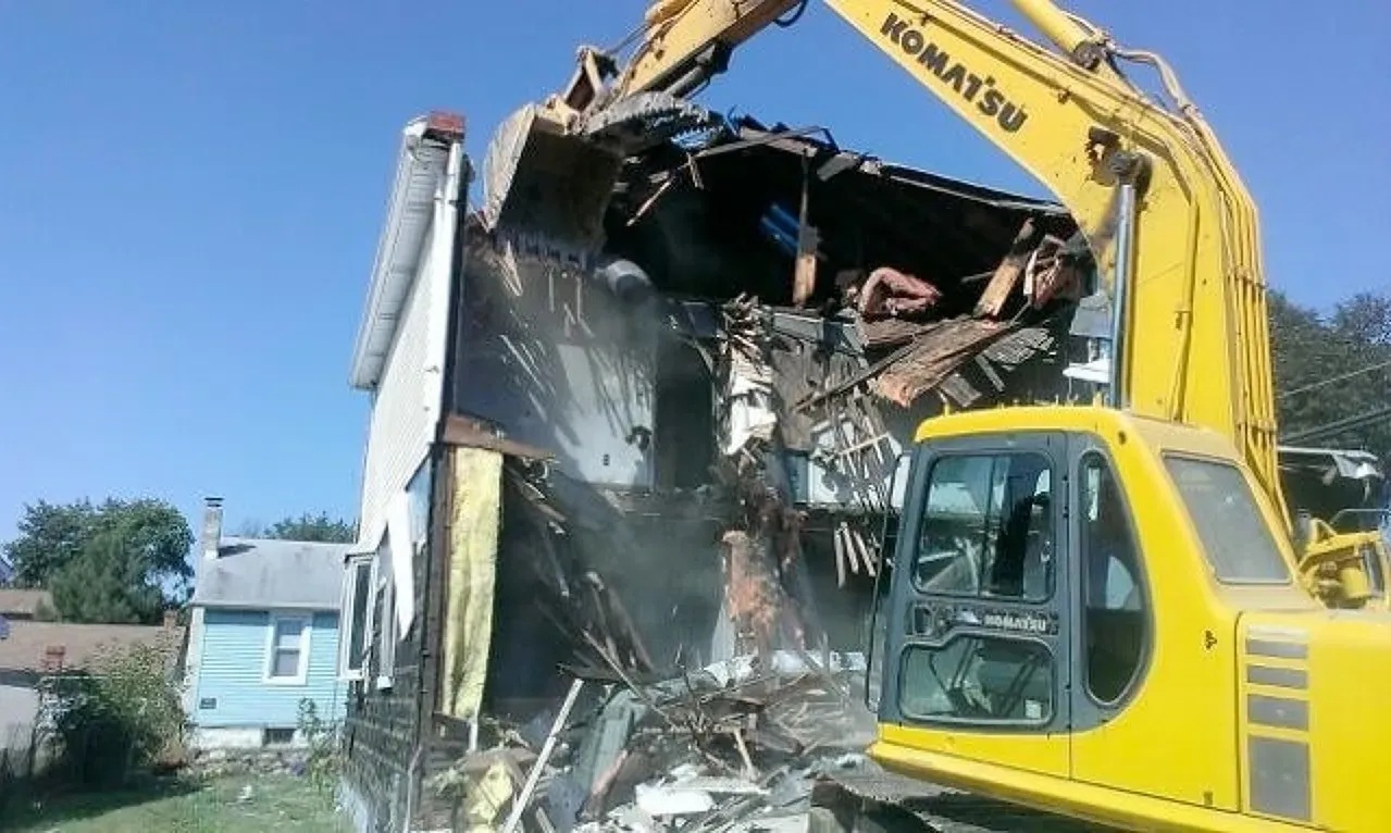 A yellow komatsu excavator is demolishing a house, shown close up.