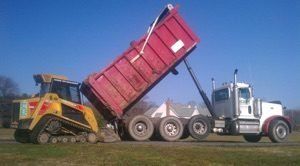 An excavation project with a dump truck is being towed by a bulldozer in a field .