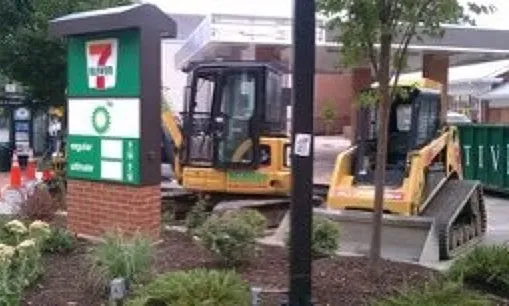 A construction vehicle is parked in front of a 7 eleven gas station.