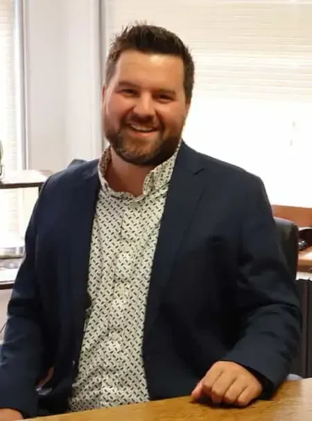 Smiling man in a navy blazer sitting at a desk in an office