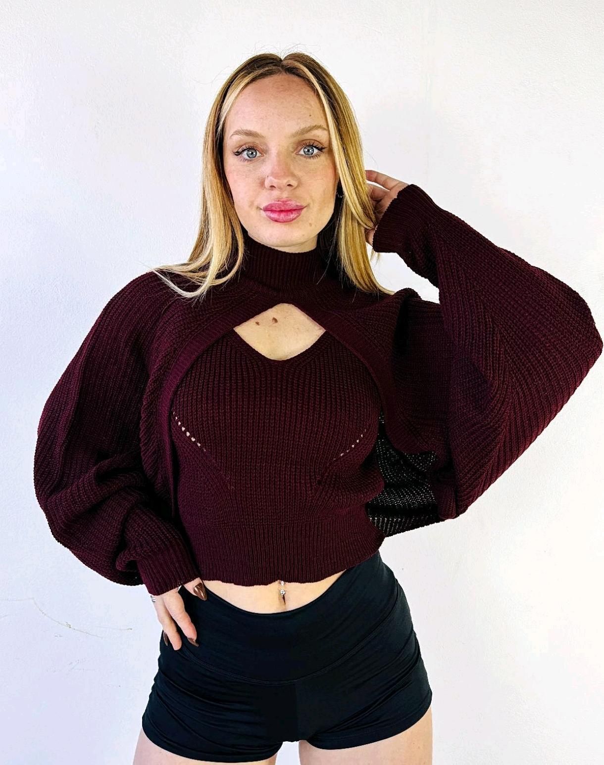 Mujer posando con un suéter color burdeos y pantalones cortos negros sobre un fondo blanco liso.