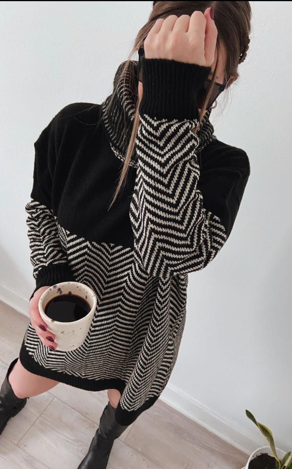 Persona con suéter de rayas blancas y negras sosteniendo una taza, posando en interiores con el rostro parcialmente cubierto.