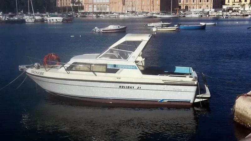 Motoscafo bianco su acque blu calme vicino a un porto con edifici sullo sfondo.