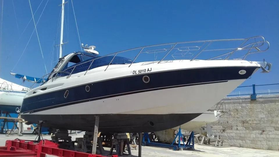 Un grande yacht a motore bianco e blu su un rimorchio in un cantiere navale sotto un cielo azzurro e limpido.