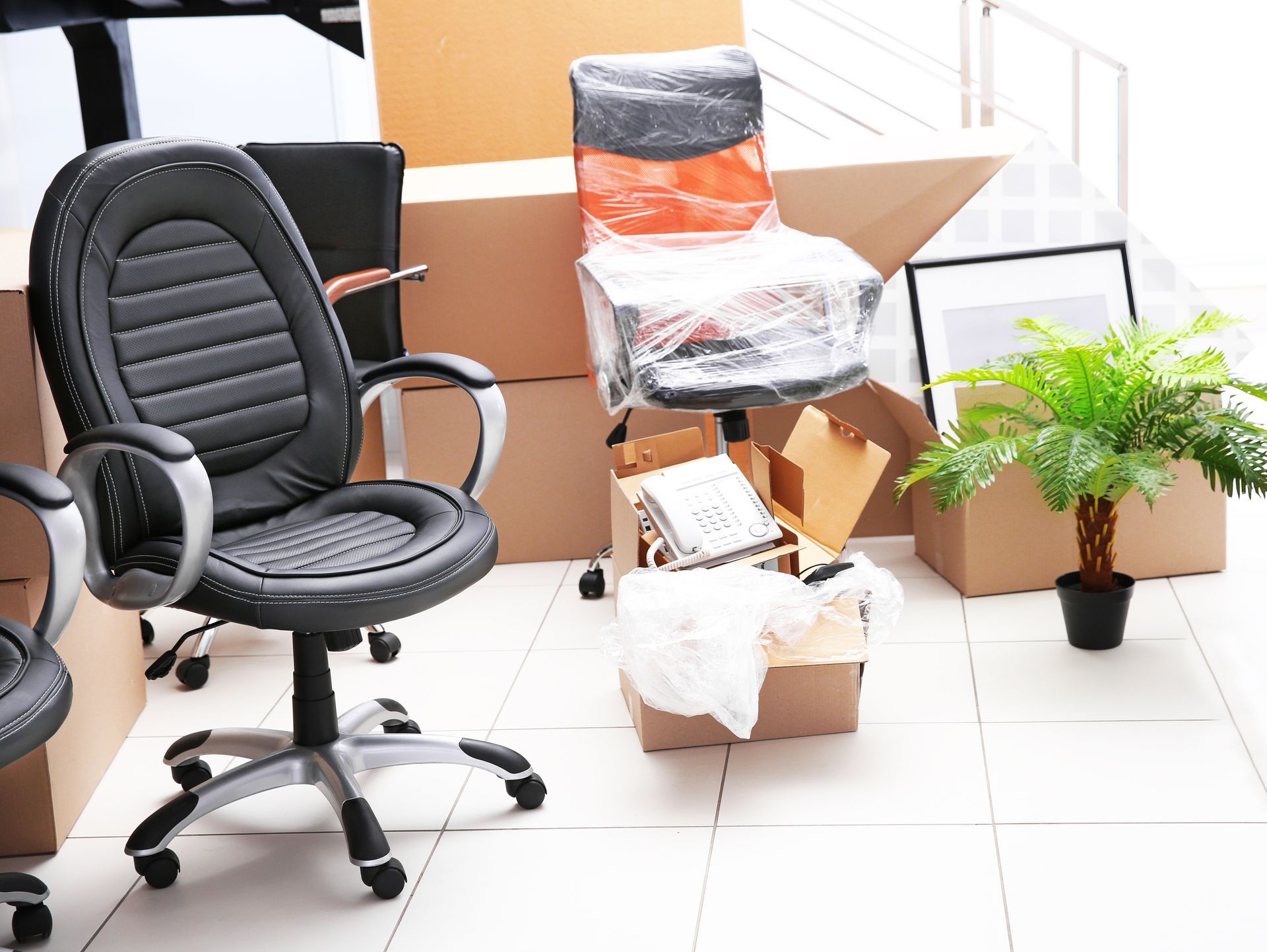 An office chair is sitting in a room surrounded by boxes and a plant.