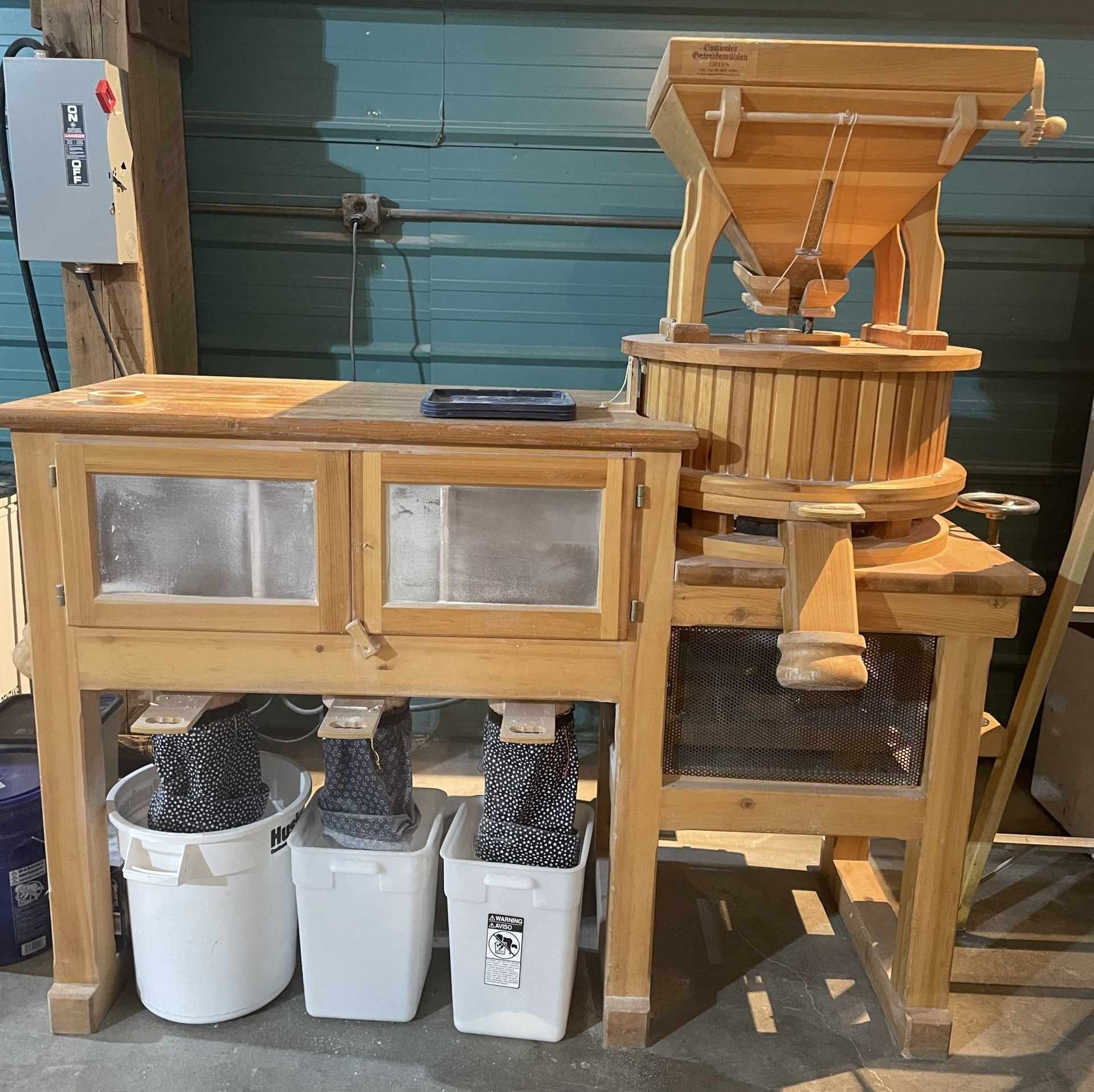 Wooden grain mill with buckets catching the milled product.