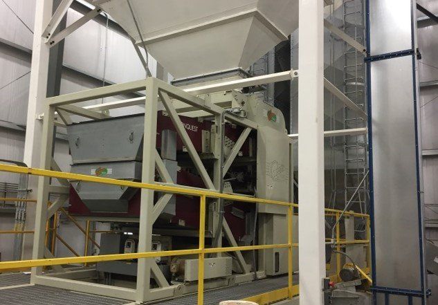 Industrial machinery with white hopper, framework, and red accents inside a warehouse.