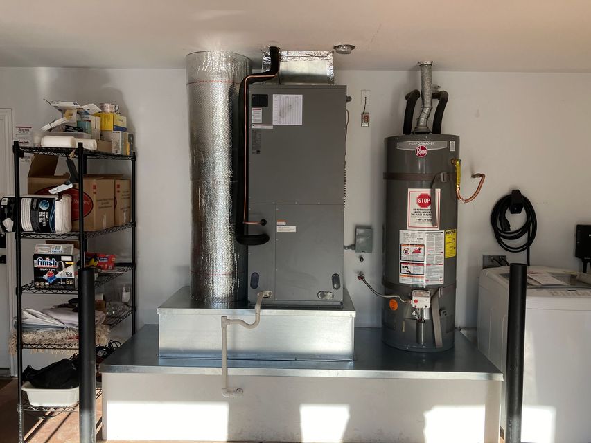 Utility room with furnace, water heater, shelving, and a dryer vent hose above a laundry area
