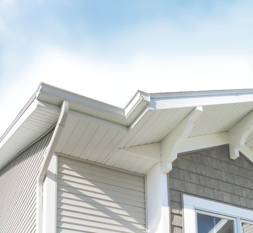 An exterior corner view of a building featuring white soffits, gutters, and siding with grey shingle wall accents.
