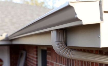 A light-colored gutter system with a downspout attached to the side of a brick building.