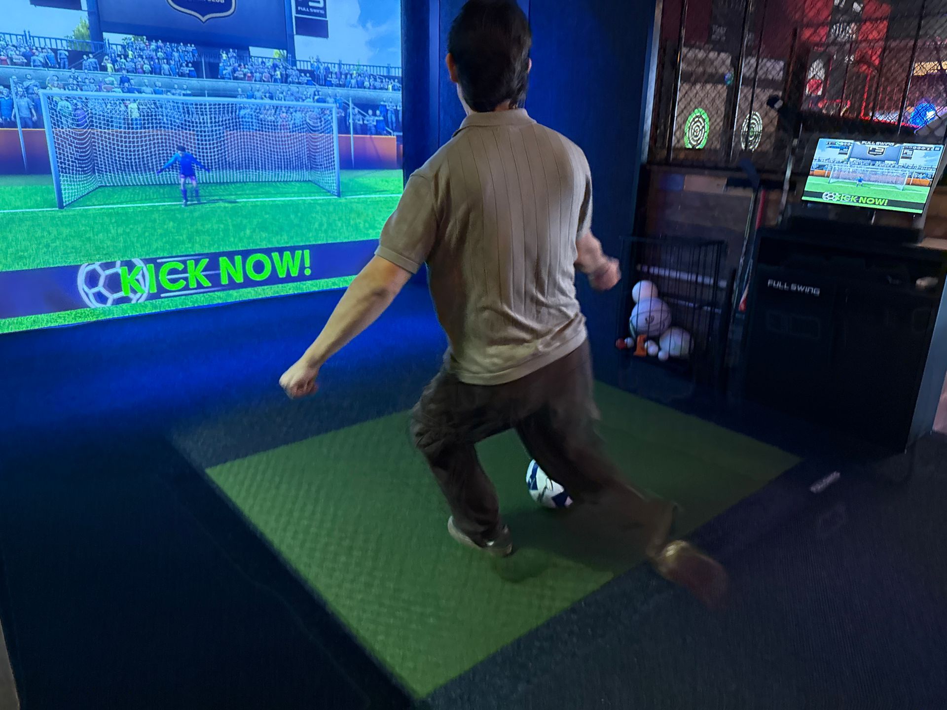 Two men at a golf simulator, looking at a screen displaying a course; one holds a golf club.