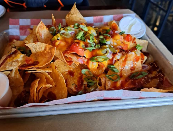 Nachos on a tray, topped with cheese, salsa, and jalapenos, with sour cream.