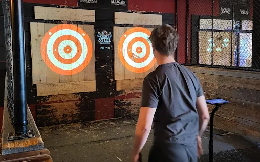 Man throws an axe at a target in an axe-throwing venue.
