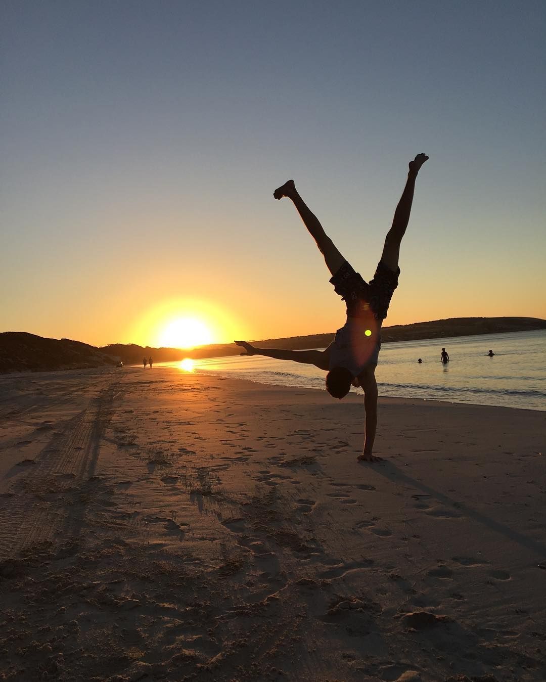 Man doing a handstand on a beach at sunset