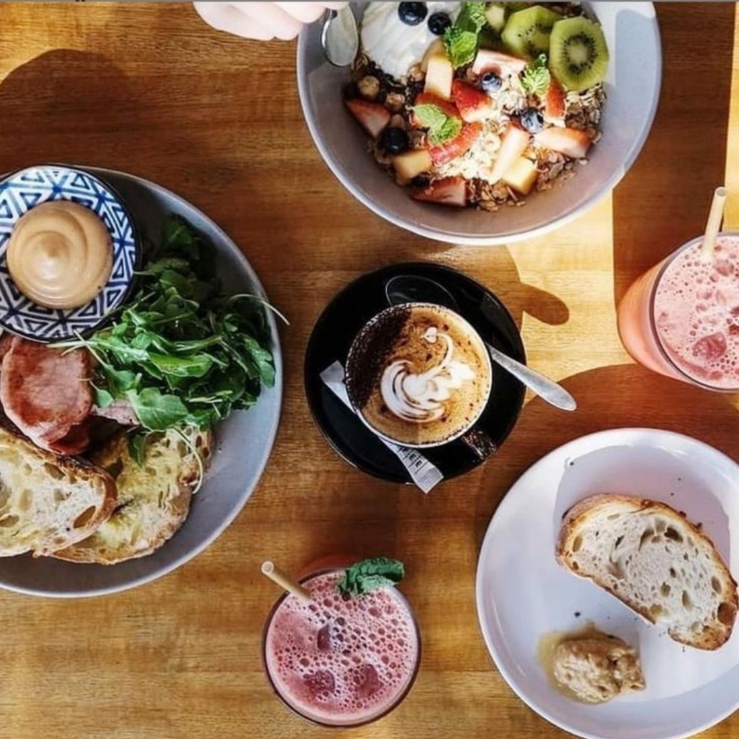 Breakfast spread: toast, fruit bowls, coffee, smoothies on a wooden table