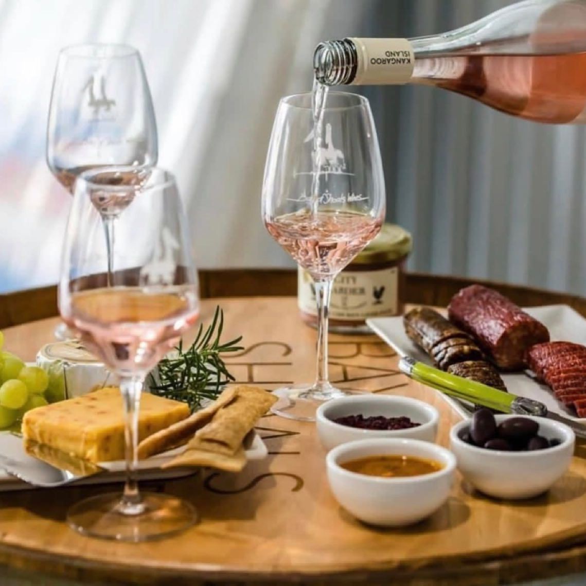 A hand pouring rosé wine into a glass with cheese, olives, and meat