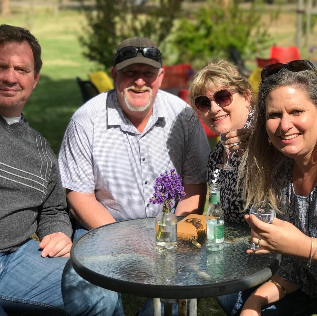 Four people smiling around a small table outdoors while holding a drinks