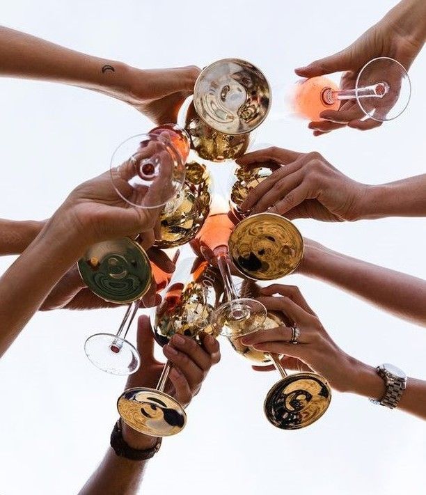 Hands clinking glasses of champagne in a toast against a bright sky.