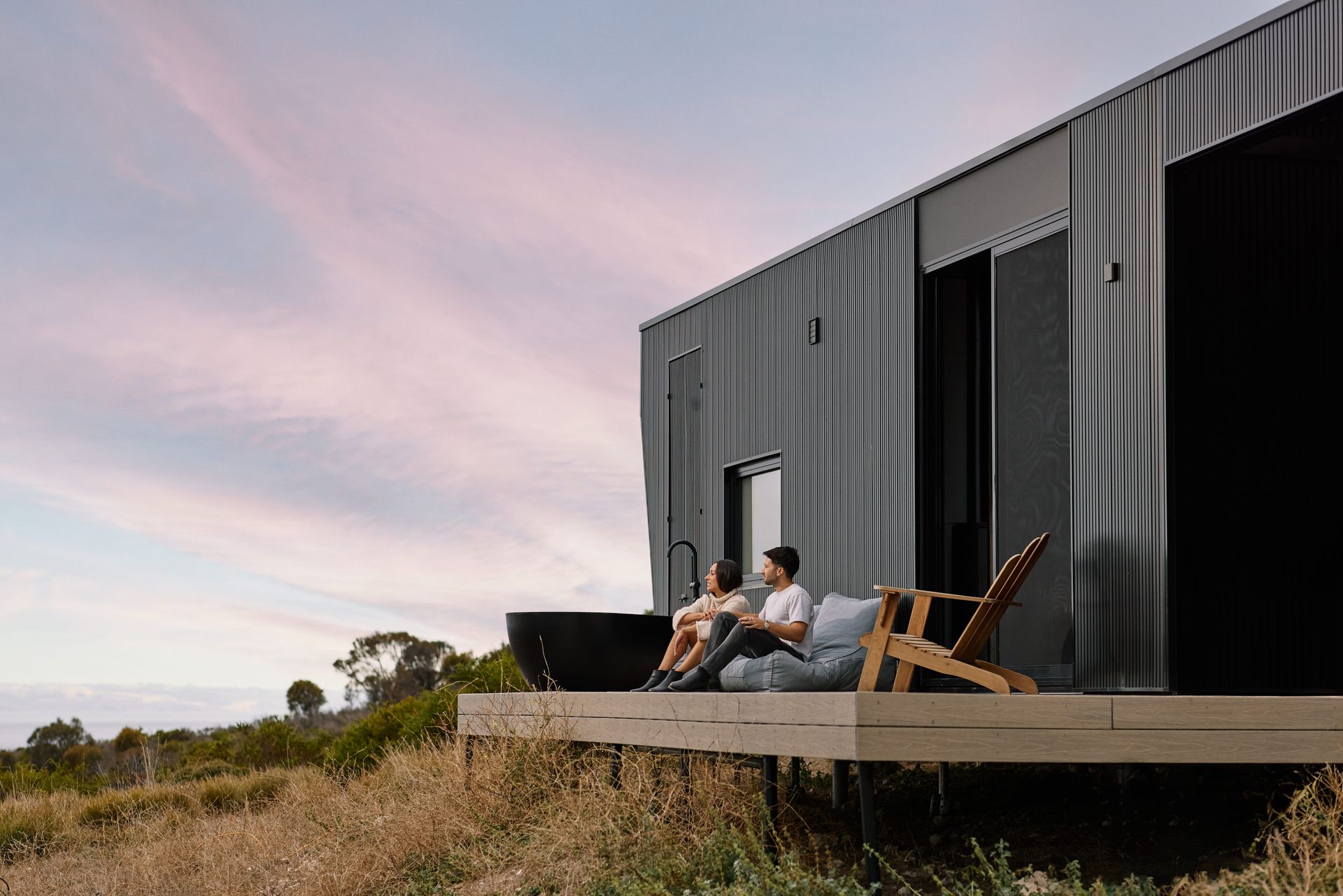 Two people relaxing on a deck beside a modern cabin at sunset