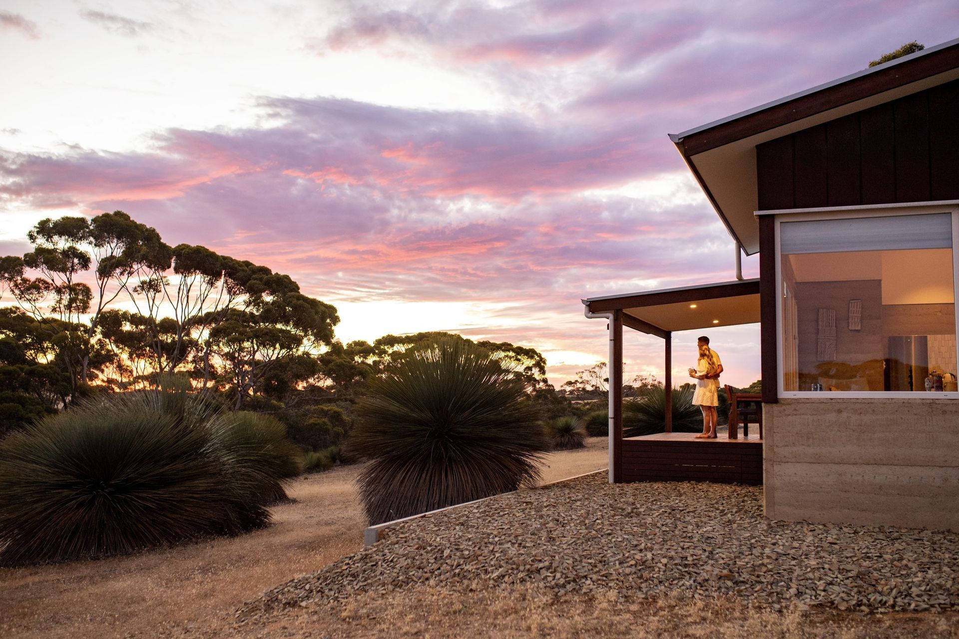 Modern house at sunset with a lit porch and gravel yard under a pink sky