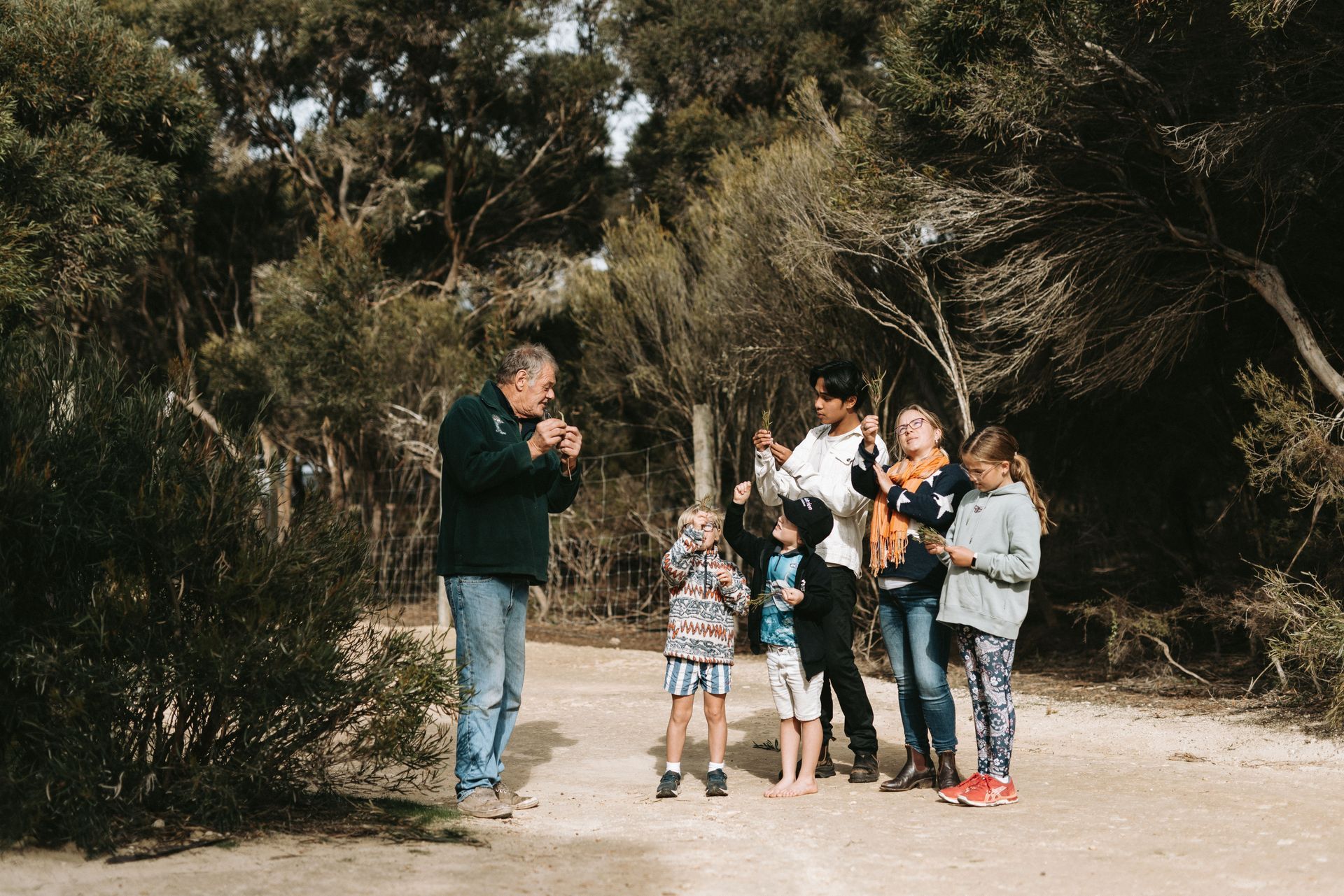 A group of people standing on a dirt path in a wooded area, some holding items up, others looking at something.