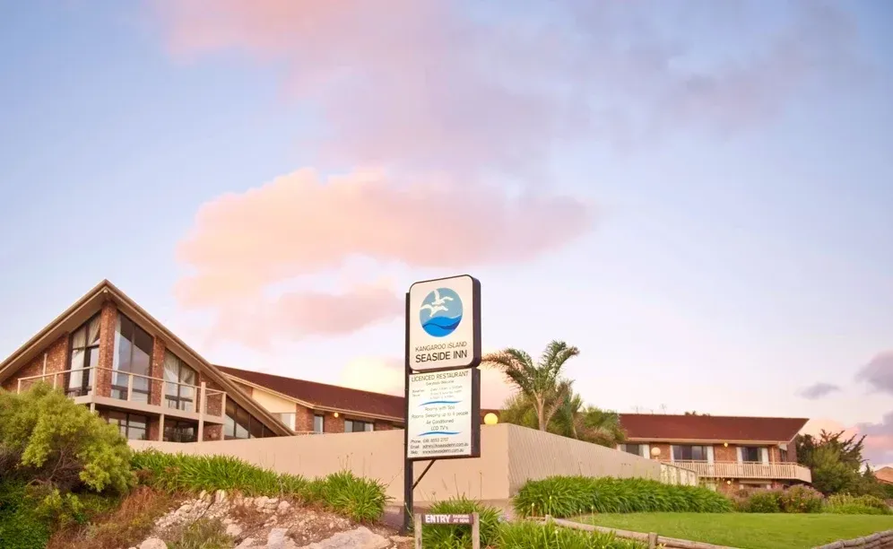 Building and roadside sign by a landscaped entrance under a pink-blue sky