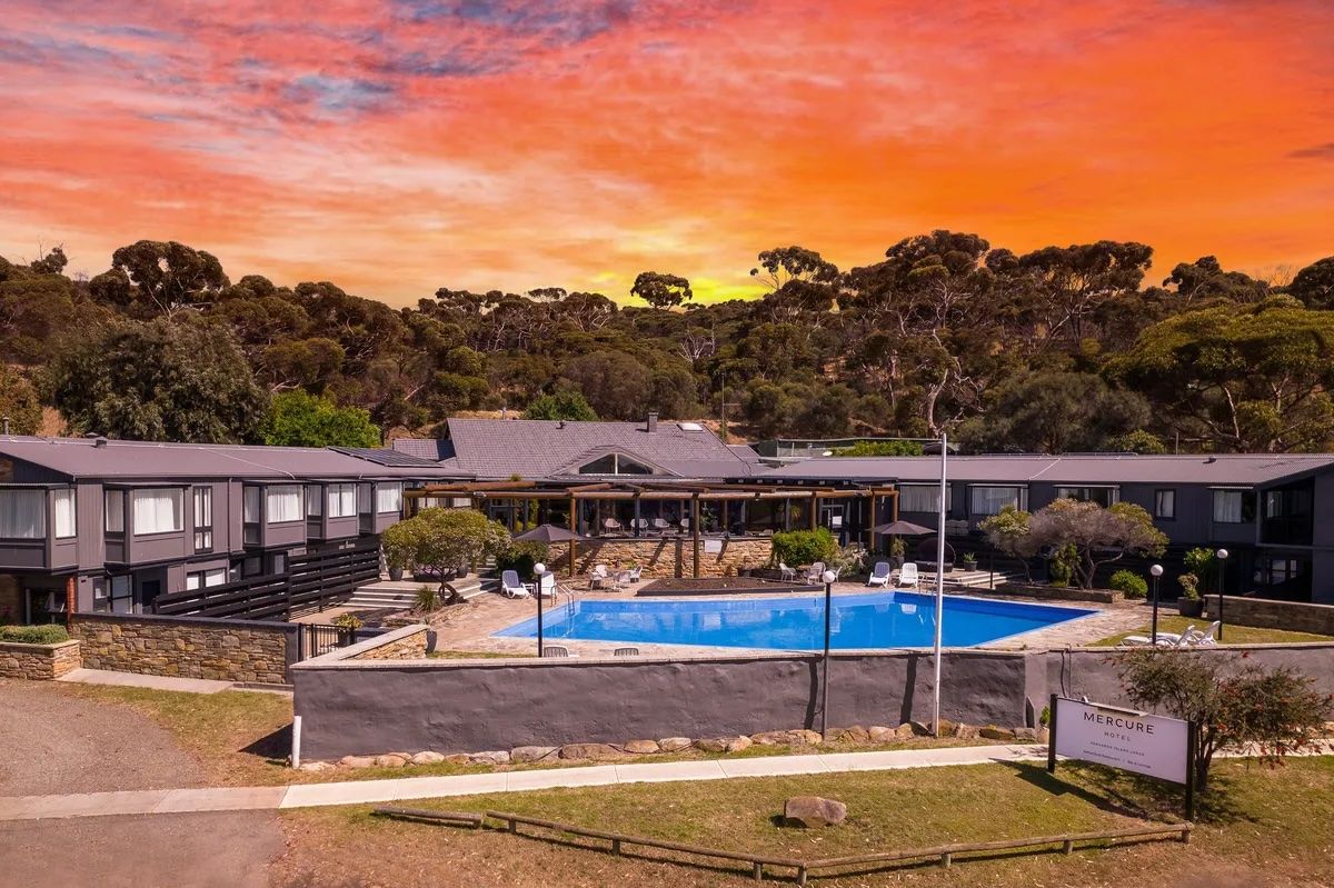 Apartment complex with a central blue pool at sunset under a colorful orange sky
