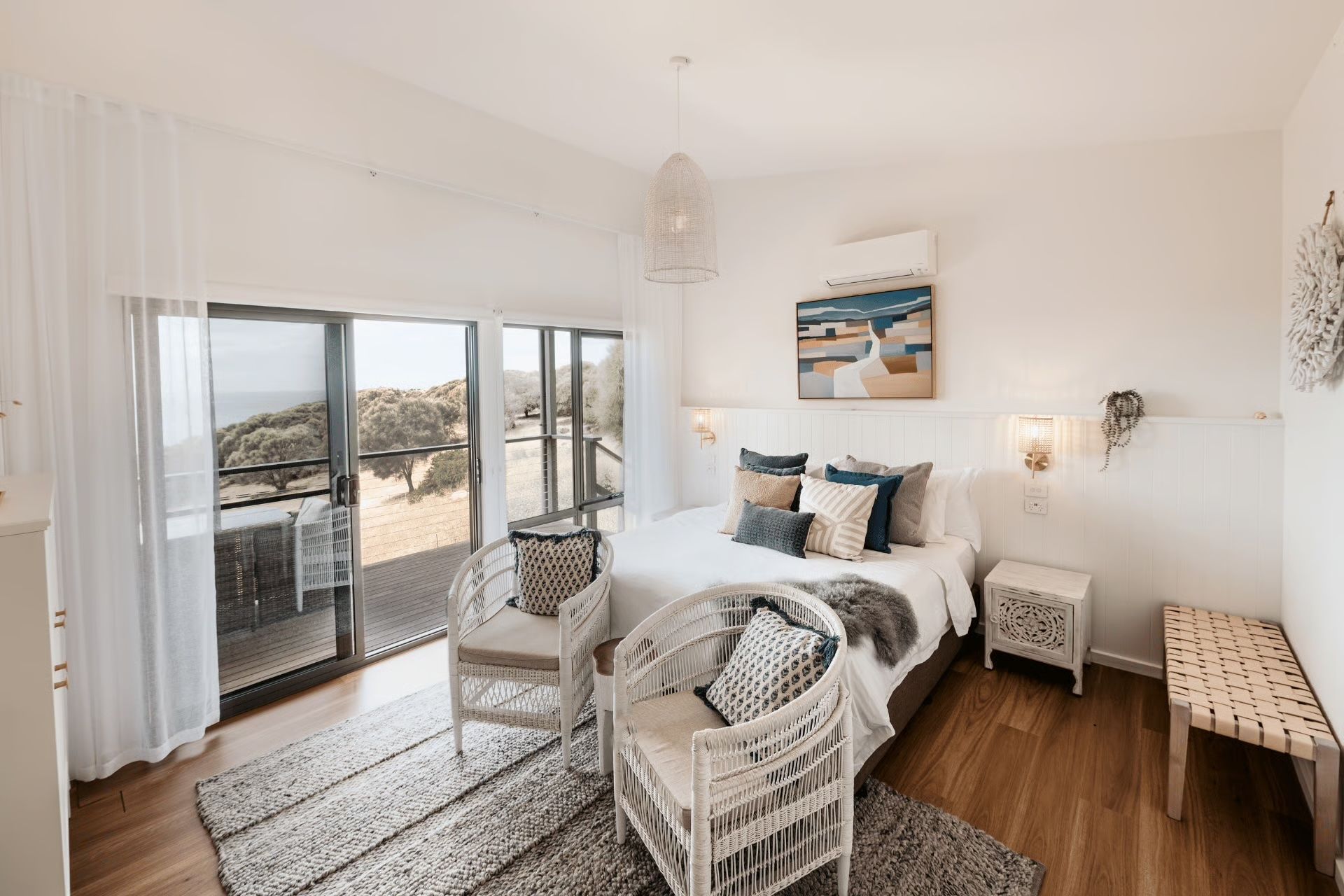 Bright white bedroom with wicker furniture, ocean view, and open balcony doors