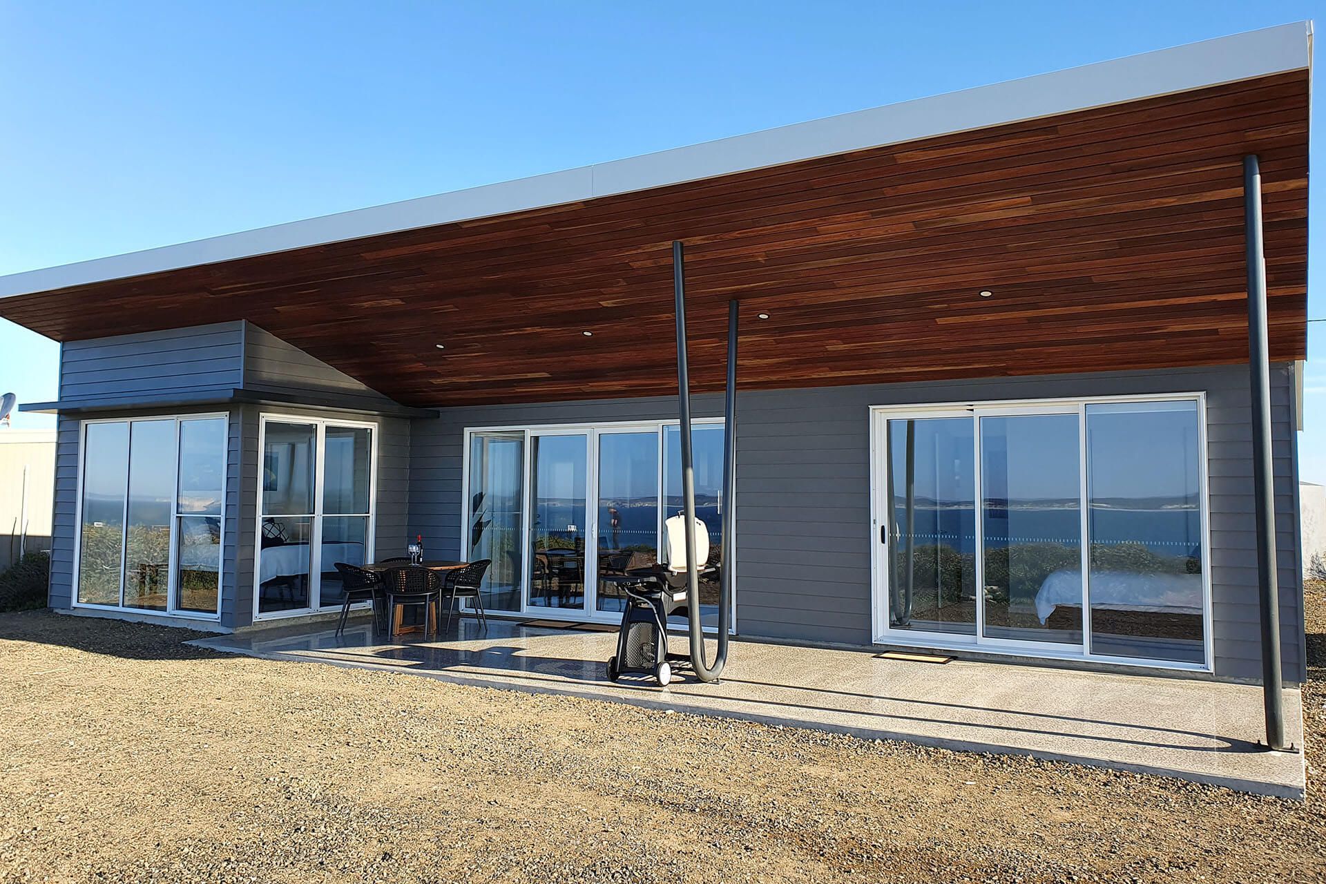 Modern single-story house with large glass doors and a slatted wooden roof over a patio