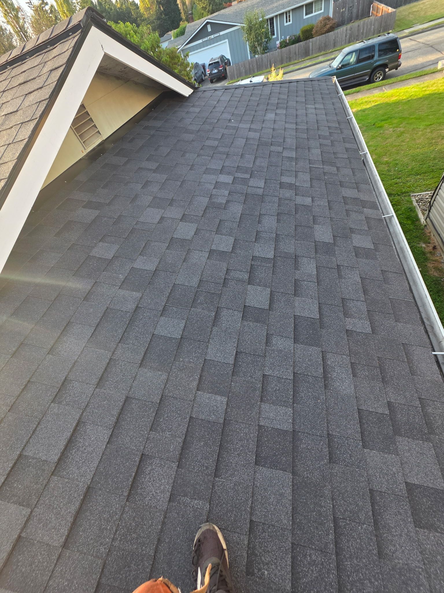 A high-angle view of a newly installed dark gray shingle roof on a residential home with a gutter visible on the side.